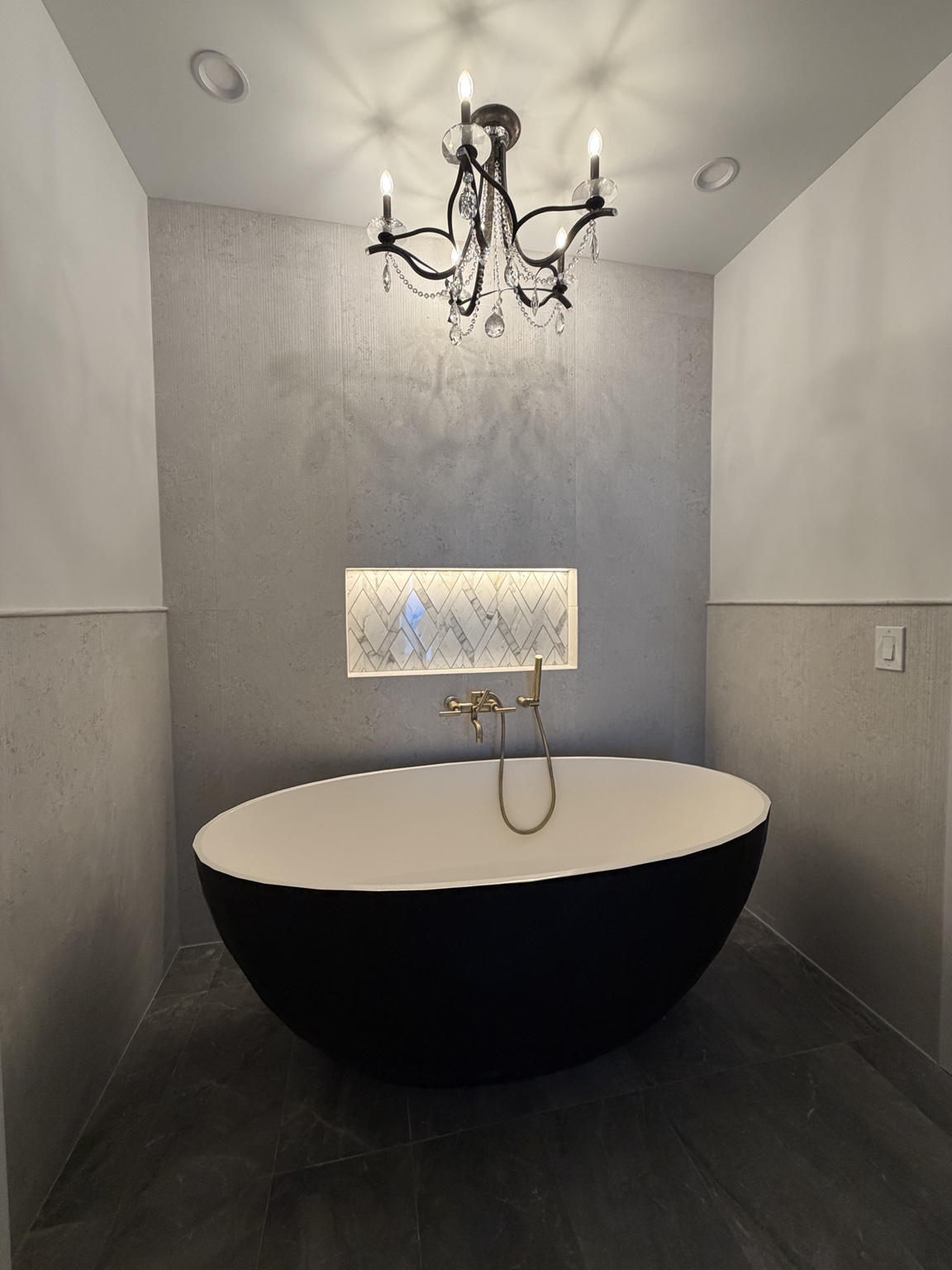 Completed freestanding bathtub installation with wall-mounted filler and handheld wand